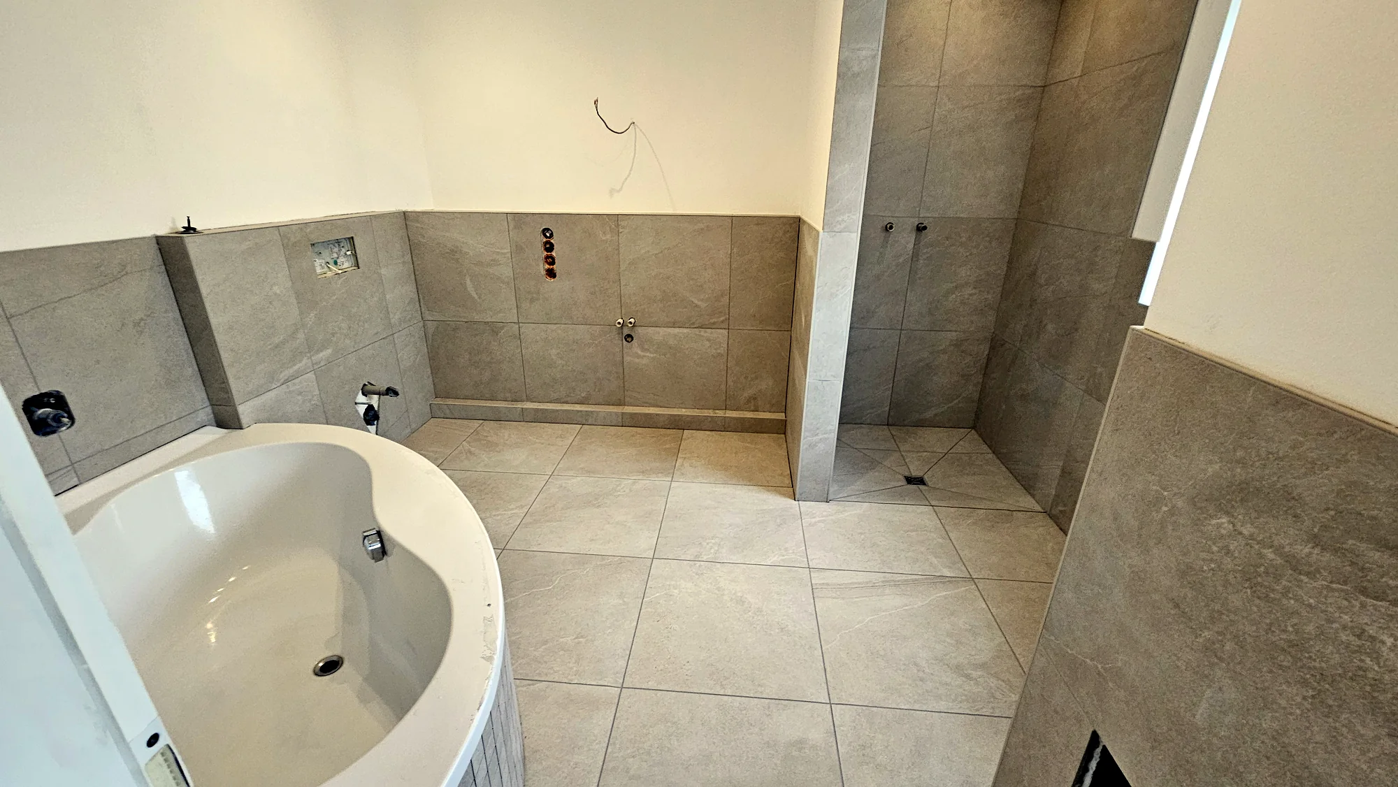 Ausgeführtes Badezimmer mit 60 mal 60 Zentimeter großen Fliesen, Mosaikbadewanne und bodengleicher Dusche